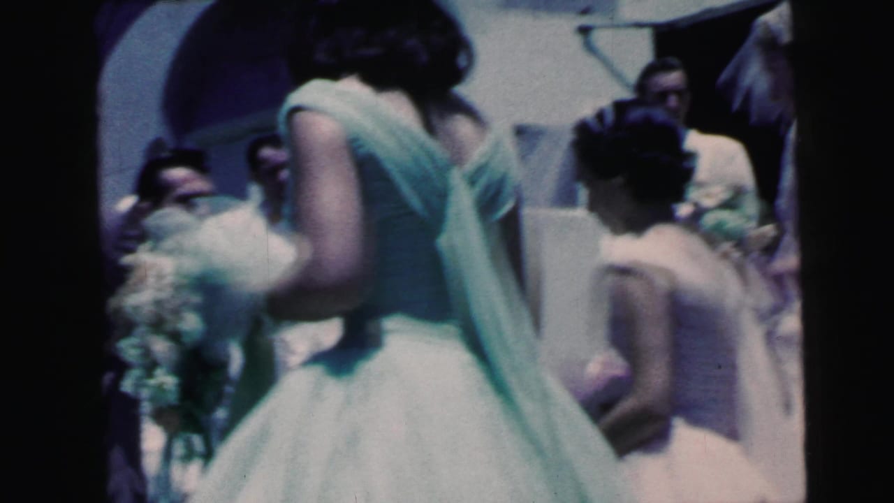 Home-movie view of a bridesmaid with bouquet in the foreground as wedding guests cluster outside the Camden ceremony entrance.