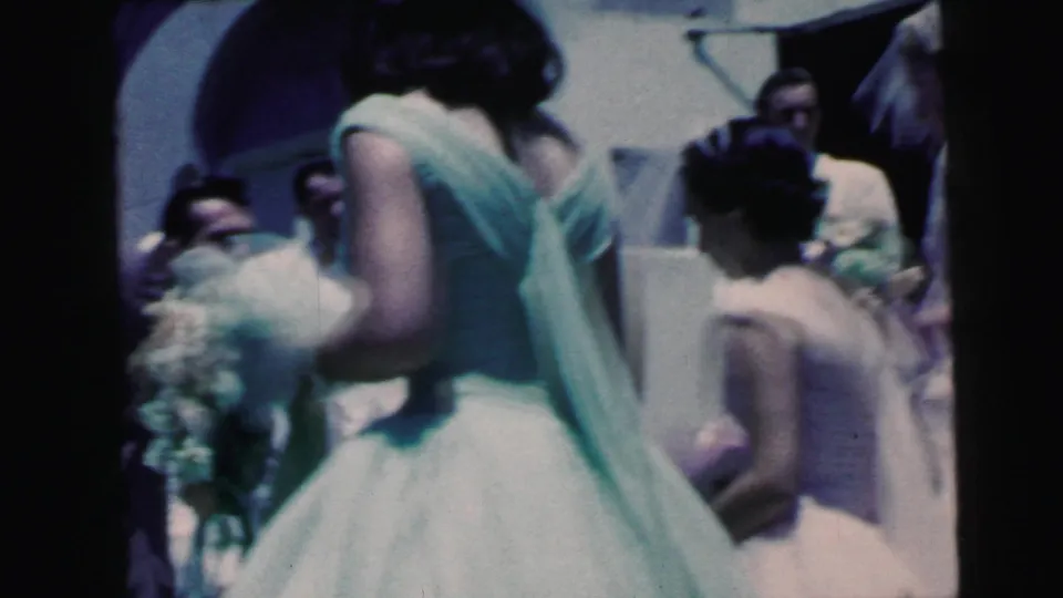 Home-movie view of a bridesmaid with bouquet in the foreground as wedding guests cluster outside the Camden ceremony entrance.