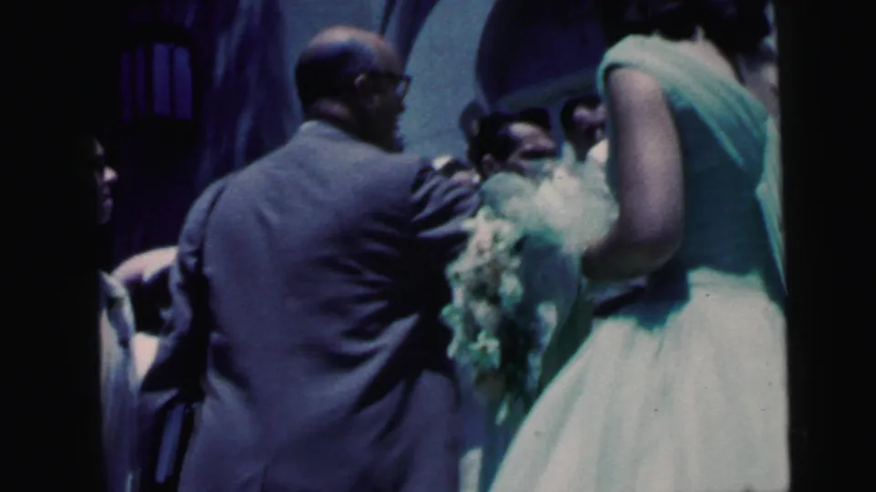 1960s wedding scene with a suited guest or relative near a bridesmaid holding a bouquet, filmed close to the church entrance.
