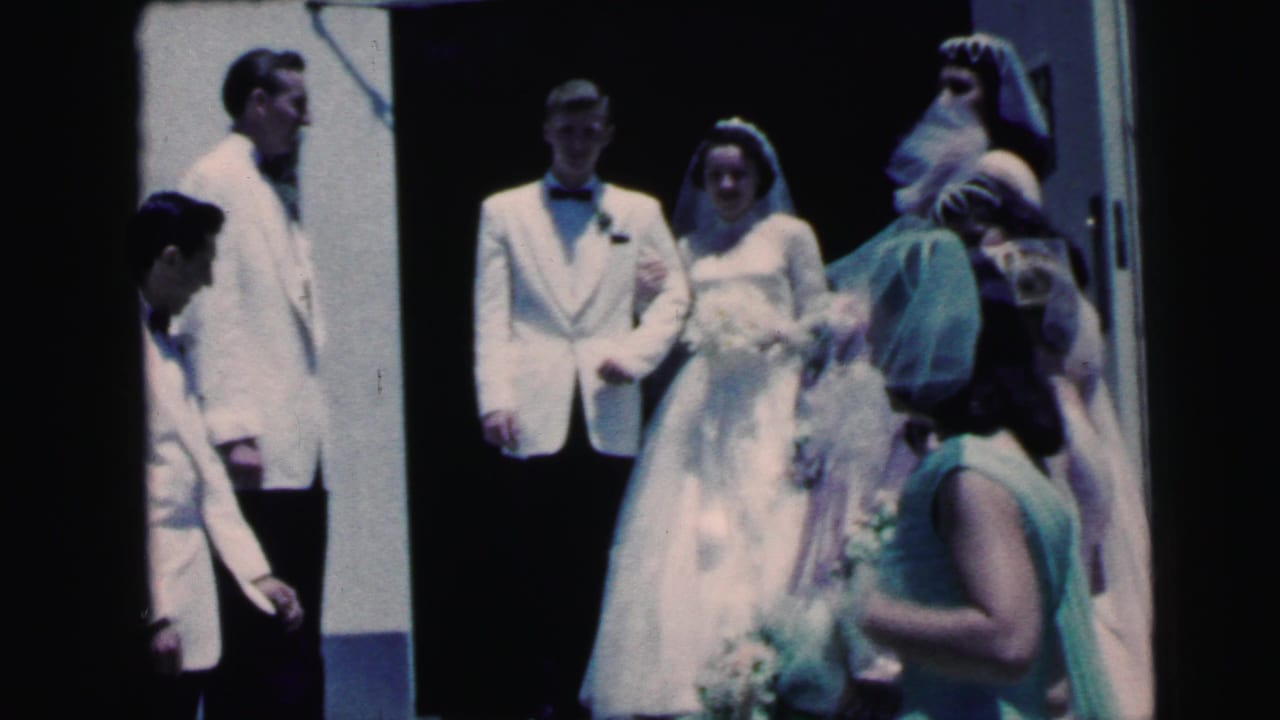 Bride and groom stand in a doorway as wedding party members gather nearby.