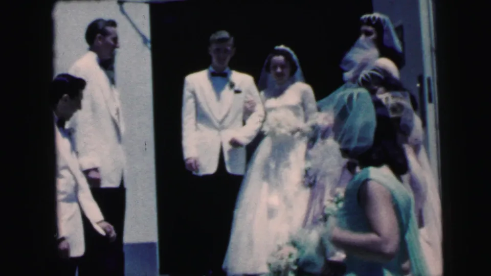1964 Camden wedding party at a doorway, with the bride and groom in white formalwear and attendants moving in front.