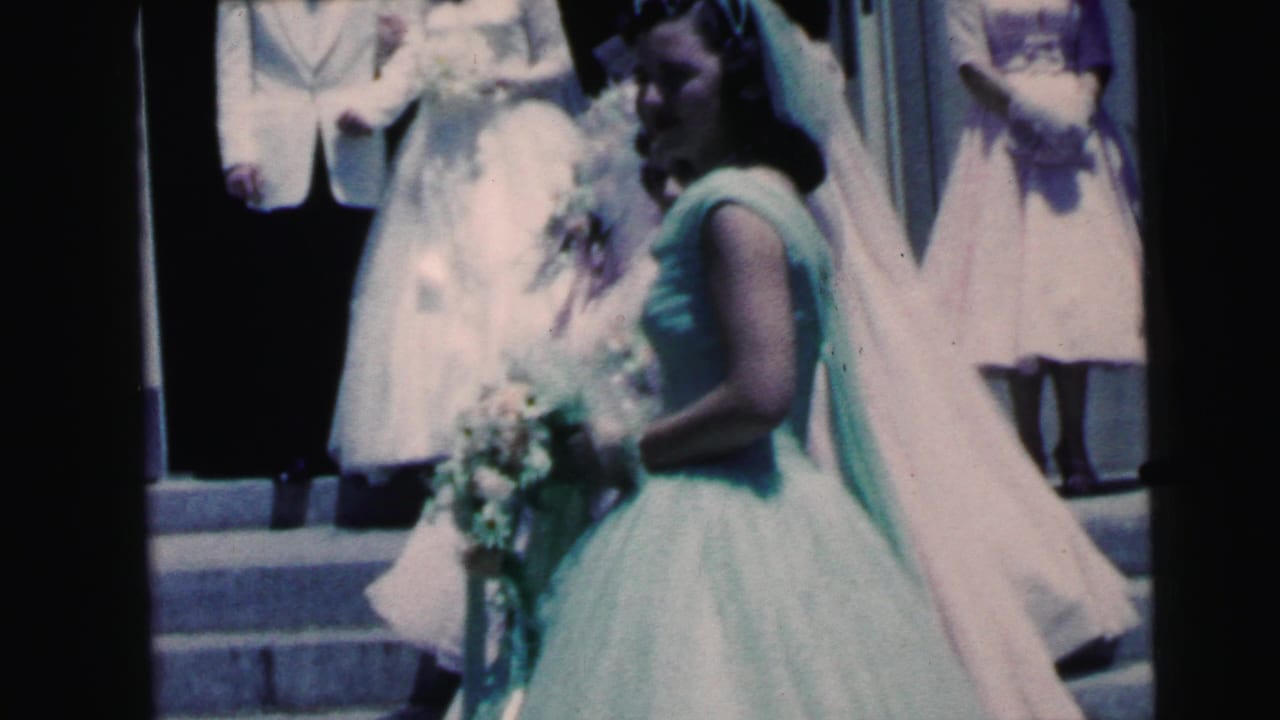 Bride in a white gown and veil beside a mint-dressed attendant on church steps.