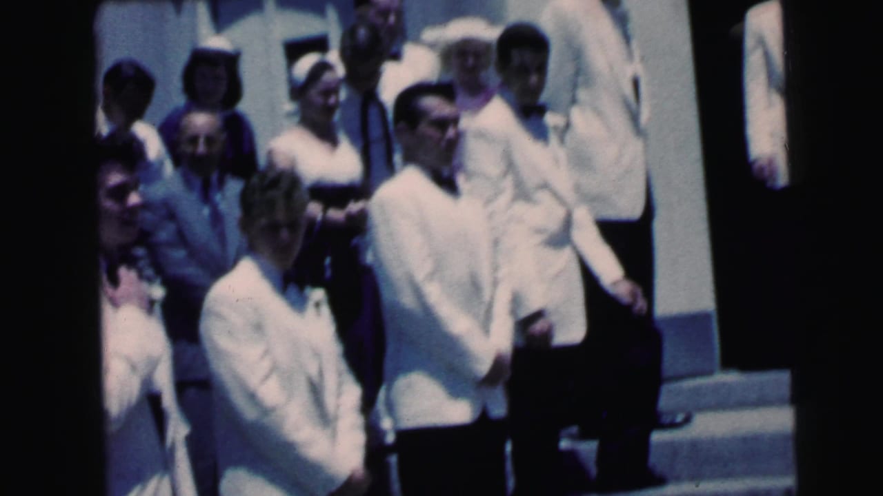 Men in white formal jackets and guests gather on church steps during the 1964 Camden wedding scene.