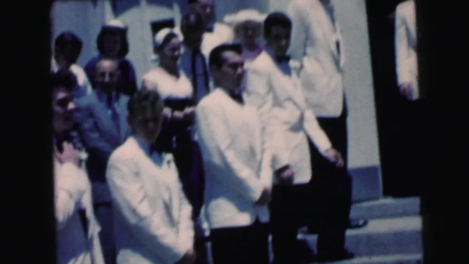 Men in white formal jackets and guests gather on church steps during the 1964 Camden wedding scene.