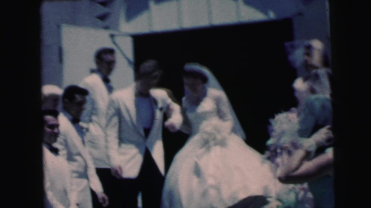 Bride and groom exit a doorway with wedding guests gathered around them.