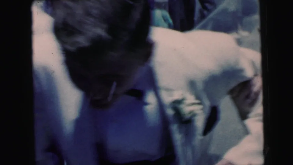 Soft, close 1964 home-movie frame of the groom and bride passing the handheld camera during the wedding exit.