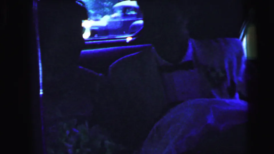 Bride and groom sit inside the car, with the window and front seat visible in cool low-light color.
