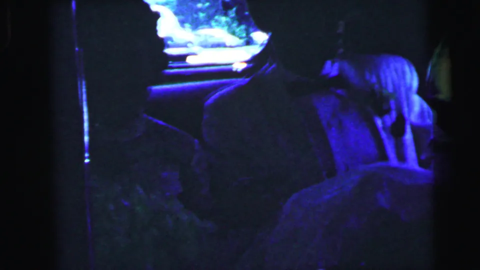 Bride and groom remain seated in the car at night, framed by the window and interior shadows.
