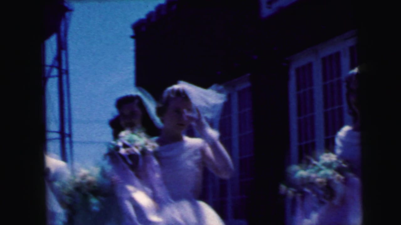 Bridesmaids in white dresses and veils stand outside a brick building with bouquets.