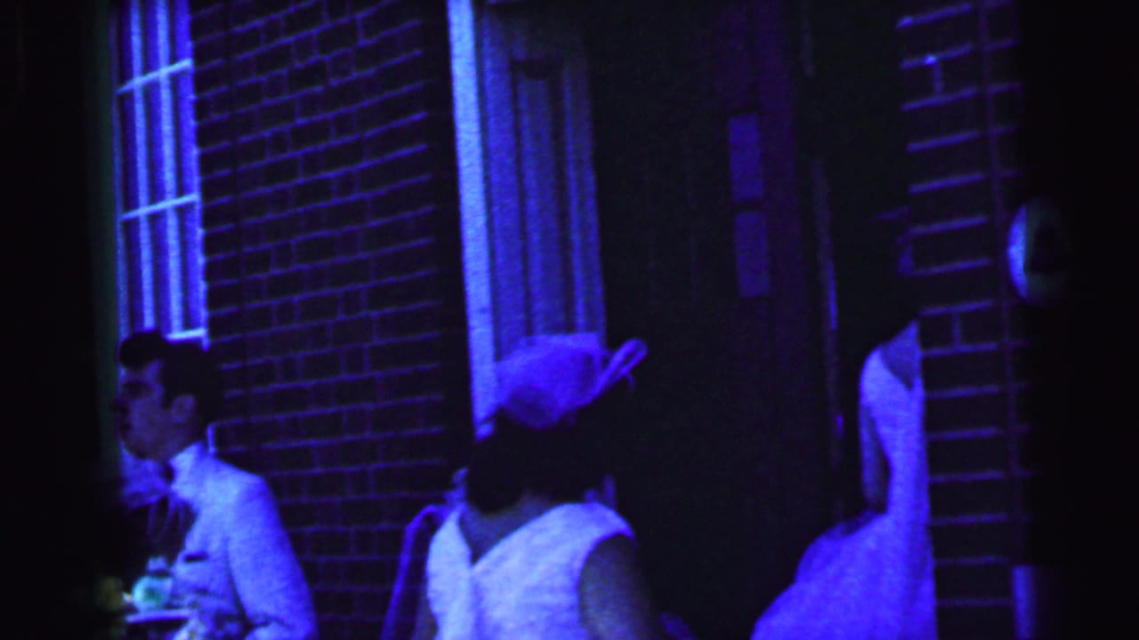 Wedding guests and attendants stand near a brick church entrance at night.