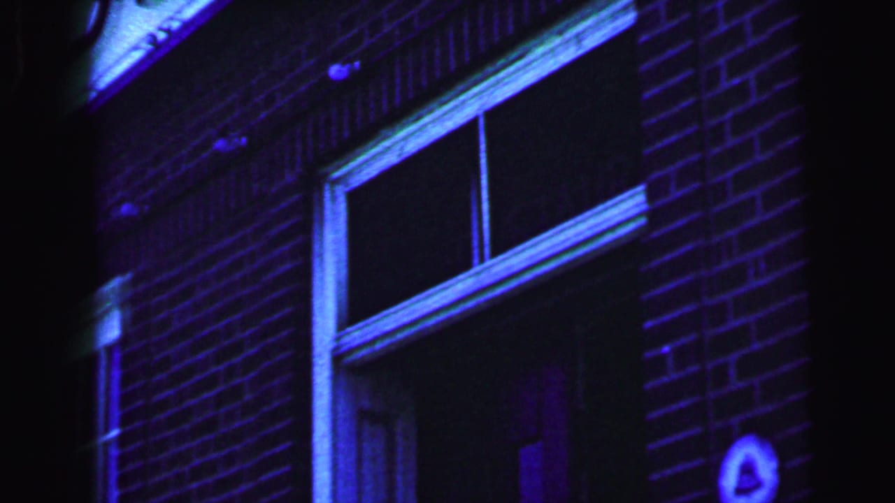 The bride and groom continue entering the brick building exterior, with a window and doorway visible in the color-shifted 1964 home movie frame.