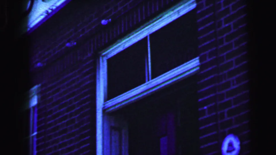 The bride and groom continue entering the brick building exterior, with a window and doorway visible in the color-shifted 1964 home movie frame.