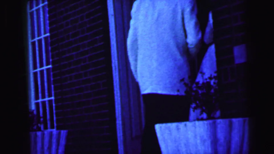 A bride in a white gown is partly seen near the brick entrance, with strong blue color shift and soft handheld 8mm framing.
