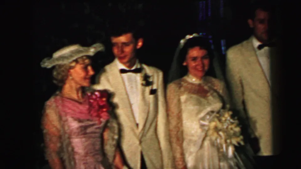 1964 Camden wedding home-movie frame showing bride, groom, and formal guests grouped for a family camera.