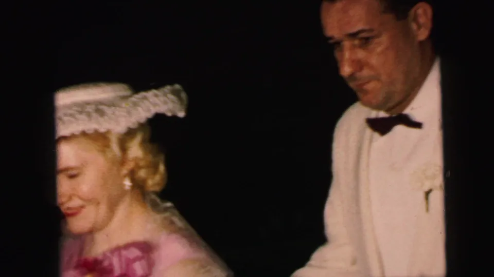 Close 8mm frame from the Camden wedding showing the formal female guest and tuxedoed man partly cropped as they pass the camera.
