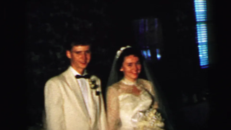 1964 Camden wedding frame showing the bride in a white lace gown and veil beside the groom in a cream tuxedo, with flowers visible.