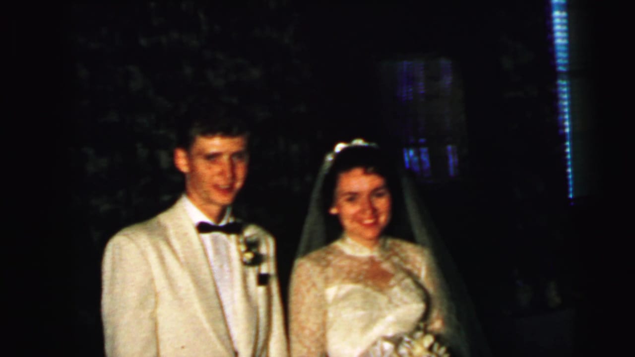 Bride and groom pose together in wedding attire against a dark background.