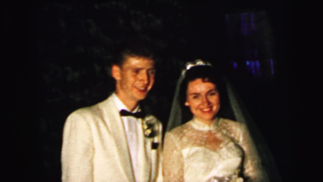 The newlyweds smile toward the camera in Camden, New Jersey, with the groom in a white jacket and the bride in a veil and lace gown.