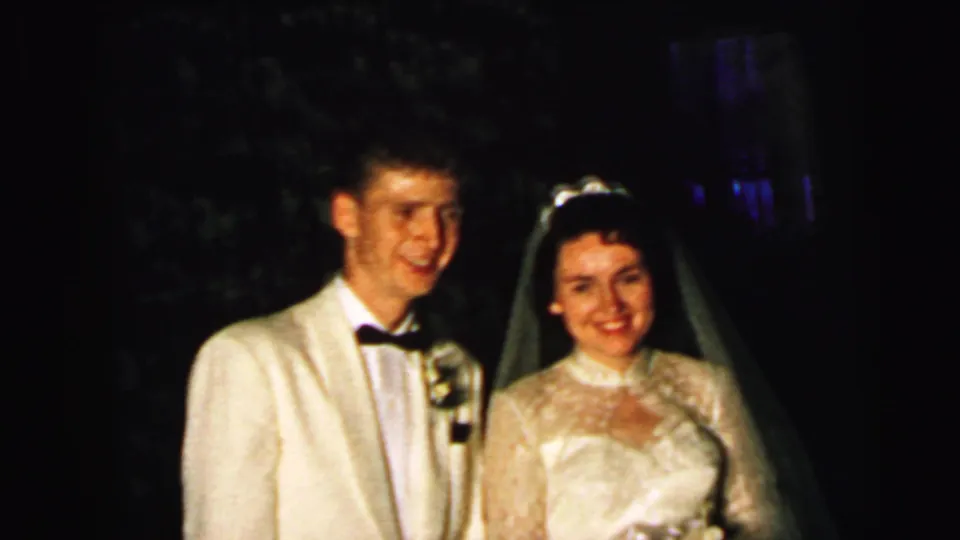 The newlyweds smile toward the camera in Camden, New Jersey, with the groom in a white jacket and the bride in a veil and lace gown.