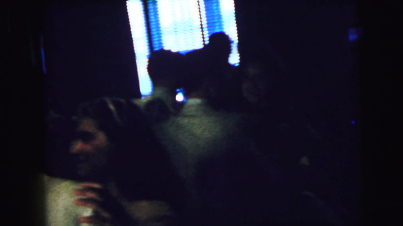 A close, shadowed 1964 Camden frame shows adults dancing together in formal clothing, with blue-lit blinds visible behind them.