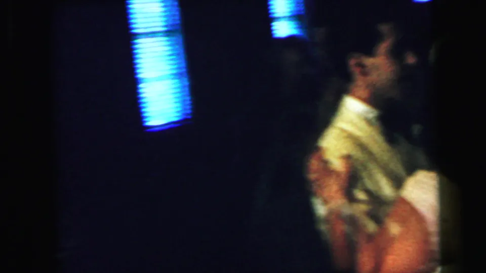 The home-movie frame shows a man in a light formal jacket dancing with a partner in a dark Camden interior in 1964.
