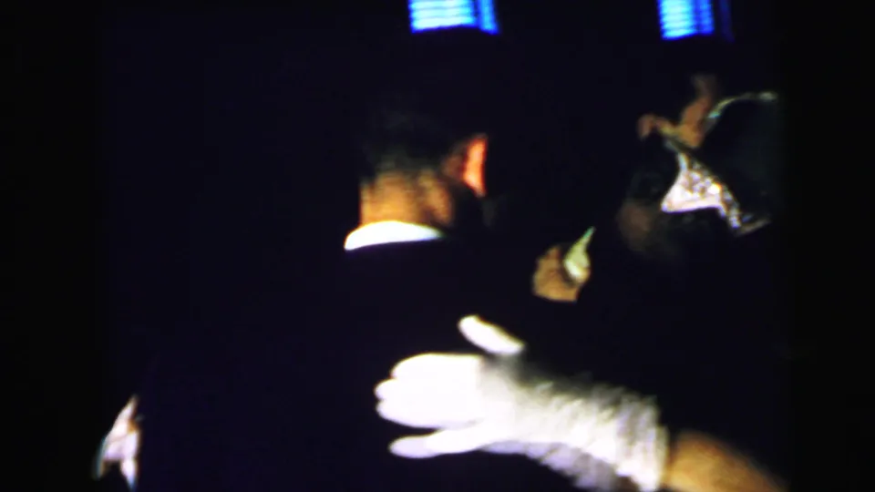 A close 1964 Camden home-movie frame shows formal dancers in deep shadow, with a bright hand or glove catching the light.
