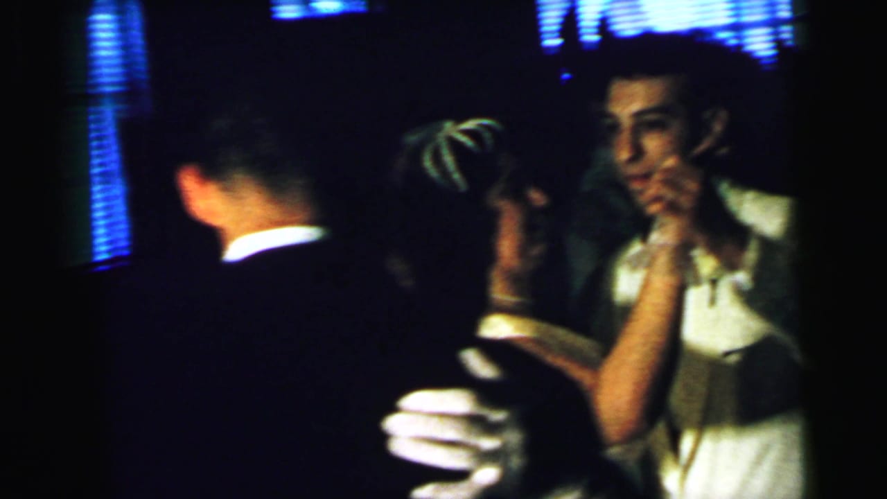 Dim 1964 Camden wedding reception frame showing adults close together, likely dancing, in soft 8mm focus.