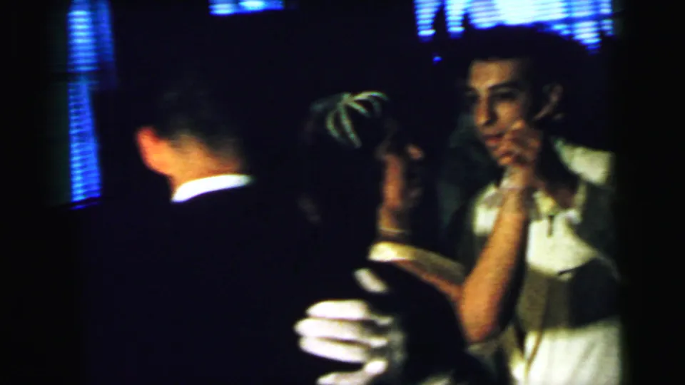 Dim 1964 Camden wedding reception frame showing adults close together, likely dancing, in soft 8mm focus.