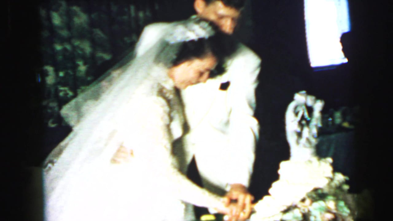 Bride in veil and groom in a light jacket cut a tiered wedding cake during a 1964 Camden reception.