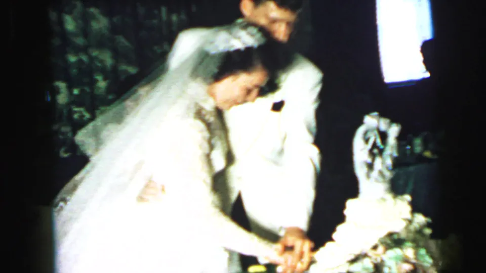 Bride in veil and groom in a light jacket cut a tiered wedding cake during a 1964 Camden reception.