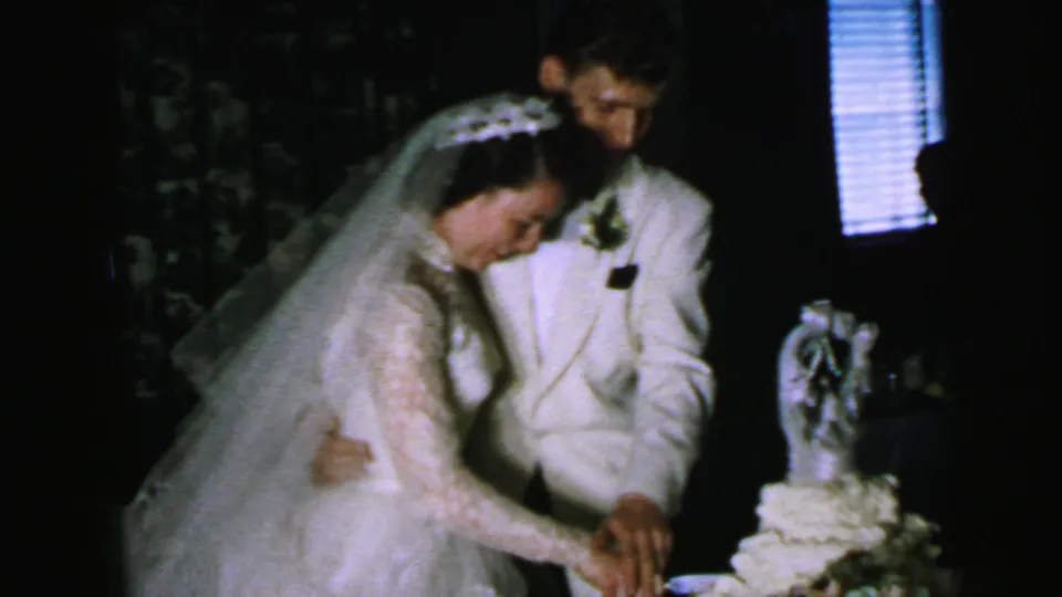 The bride and groom hold the knife together beside a tiered cake in this 1964 Camden 8mm wedding scene.