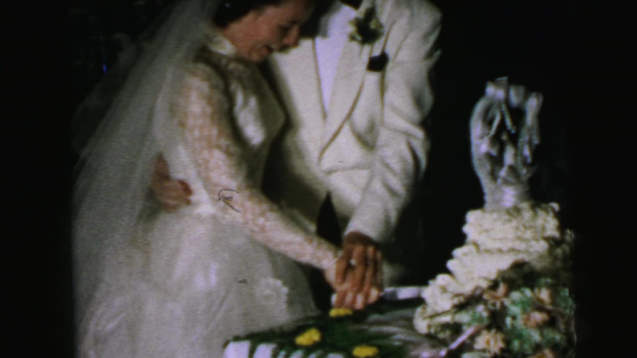 The Camden bride and groom keep their hands together on the knife beside a decorated wedding cake in dim reception light.