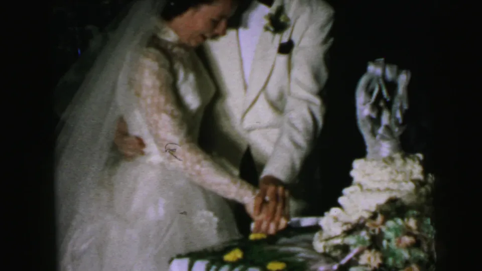 The Camden bride and groom keep their hands together on the knife beside a decorated wedding cake in dim reception light.