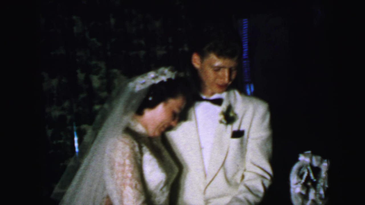 Bride and groom stand beside a wedding cake during the cake-cutting moment.