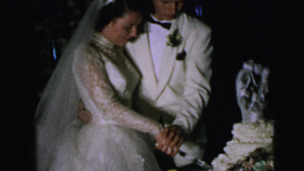 In 1964 Camden wedding home-movie footage, a bride in a lace gown and veil and a groom in a white jacket begin cutting their cake.