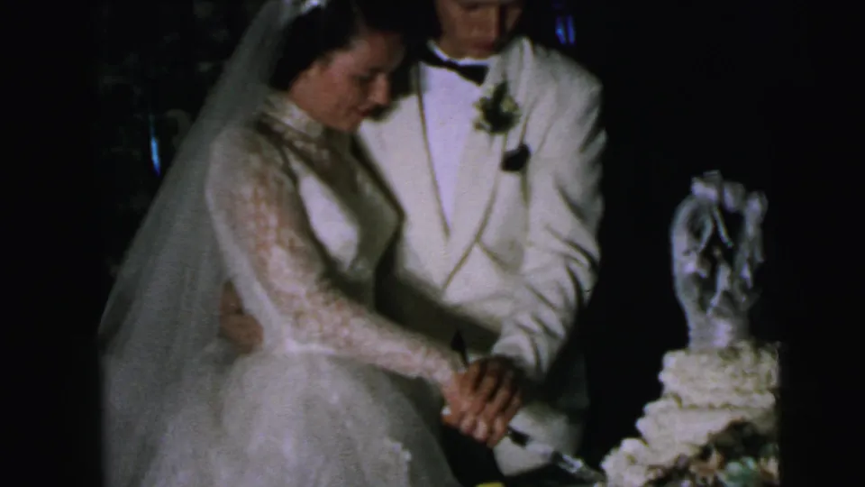 In 1964 Camden wedding home-movie footage, a bride in a lace gown and veil and a groom in a white jacket begin cutting their cake.
