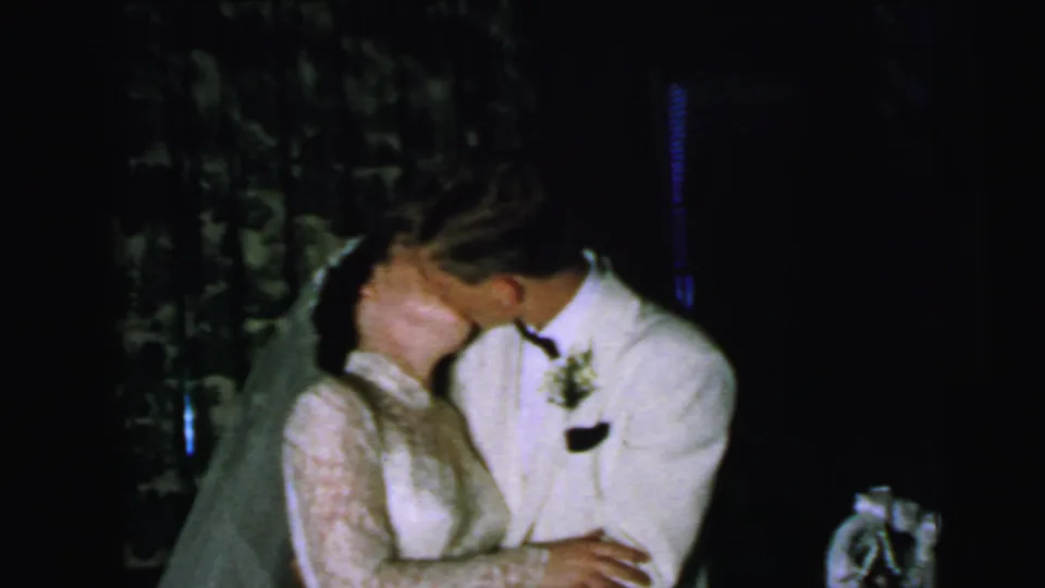 In Camden, New Jersey wedding home-movie footage from 1964, a bride in a lace gown and veil kisses a groom in a white tuxedo jacket.