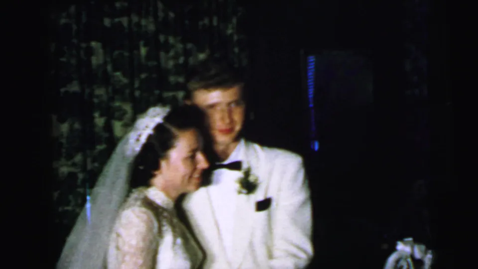 At the end of the Camden wedding clip, the bride leans close to the groom while he looks toward the camera in a dim private interior.