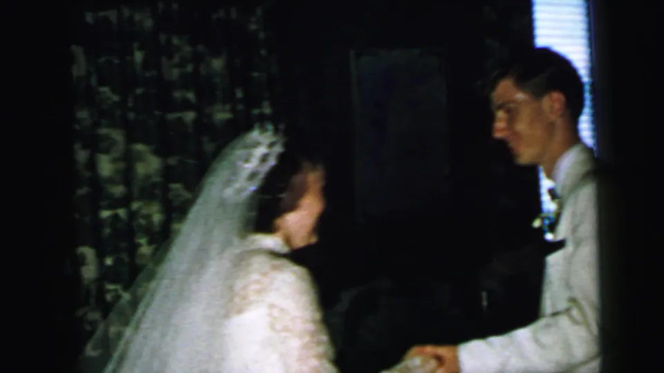 The newlyweds stand facing each other in a dim Camden interior, the bride in a veil and the groom in a white tuxedo.