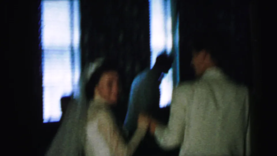 The bride turns back in motion while holding hands with the groom, seen in soft-focus 1964 home-movie footage.