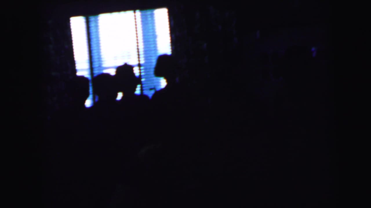 1964 Camden wedding reception footage shows silhouetted guests gathered near bright window blinds in a dim room.