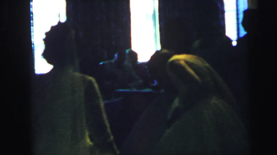 The bride, wearing a white gown and veil, appears among guests in a dim 1964 Camden wedding reception scene.