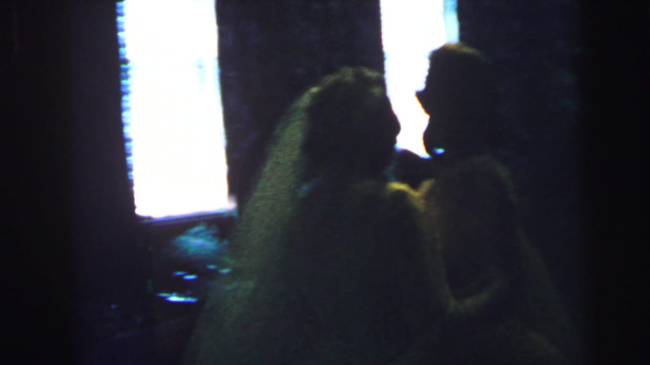 In 1964 Camden wedding footage, a veiled bride leans toward a guest or partner in a dim, backlit reception interior.