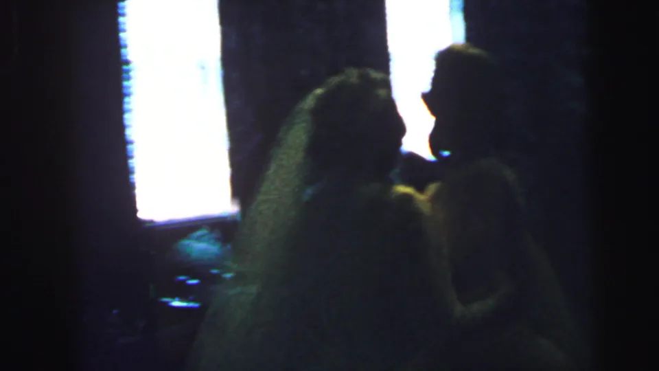In 1964 Camden wedding footage, a veiled bride leans toward a guest or partner in a dim, backlit reception interior.