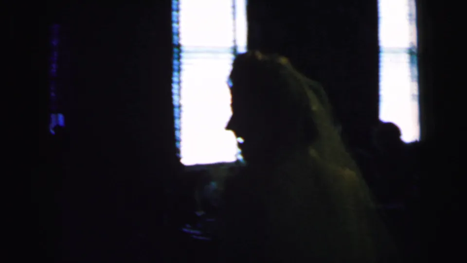 A long-haired reception guest appears in silhouette against bright window light in the 1964 Camden wedding home movie.