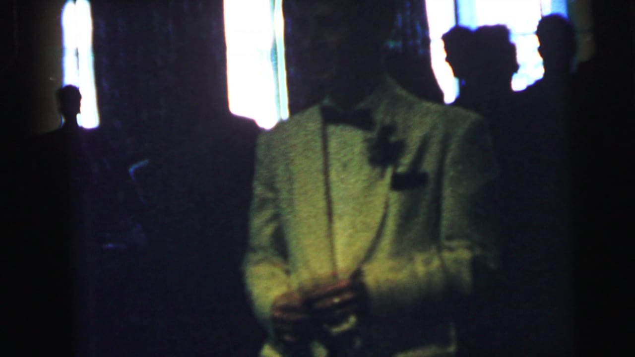 In a Camden, New Jersey 1964 home-movie frame, a man in a white tuxedo jacket stands backlit among shadowed guests.