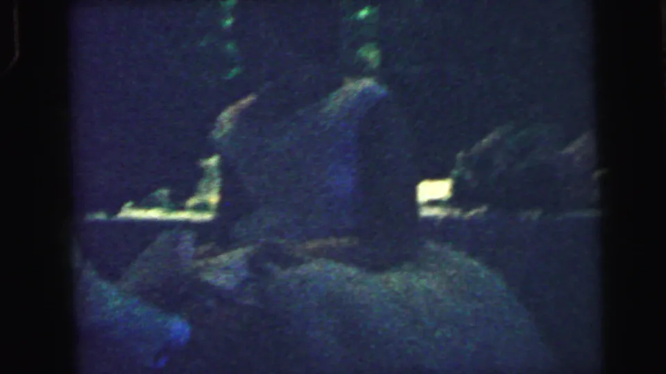 1964 Camden wedding reception footage showing a suited figure near the bride, with guests barely visible in the dim 8mm frame.