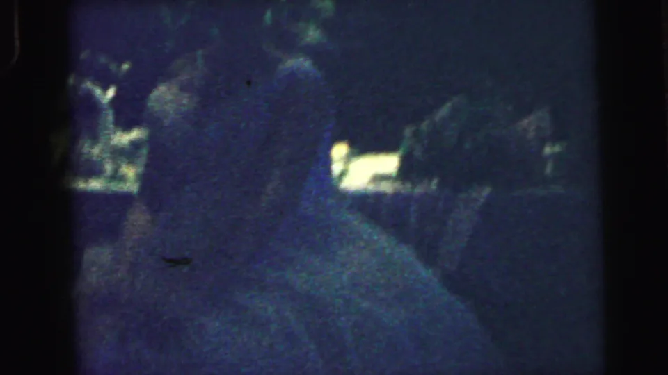 1964 Camden, New Jersey home-movie frame of the wedding garter moment, with the couple and nearby guests obscured by low light.