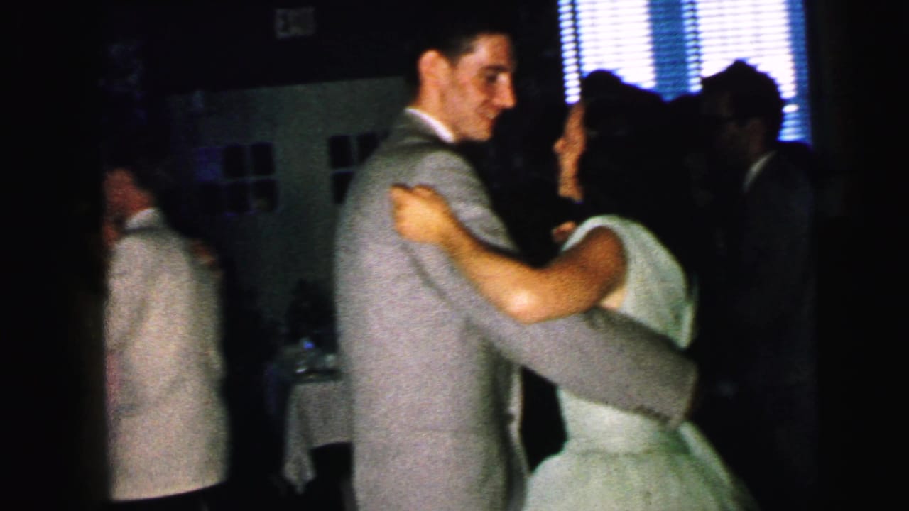 1964 Camden home-movie frame of a couple dancing close together in a dark interior, with other guests partly visible.