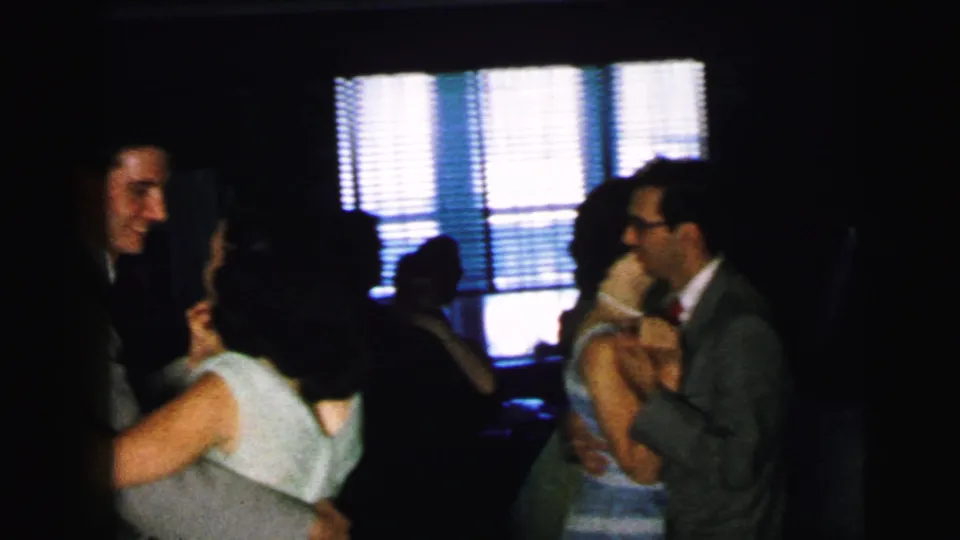 1964 Camden home-movie frame showing multiple adults dancing at a formal indoor party, filmed with soft focus and low light.